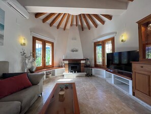 Ein geräumiges Wohnzimmer mit Kamin, Fernseher und Holzbalken an der Decke.