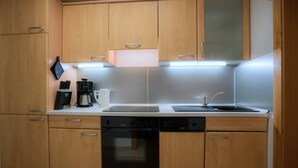Una cocina compacta con muebles de madera, un lavavajillas negro, una estufa y una cafetera.