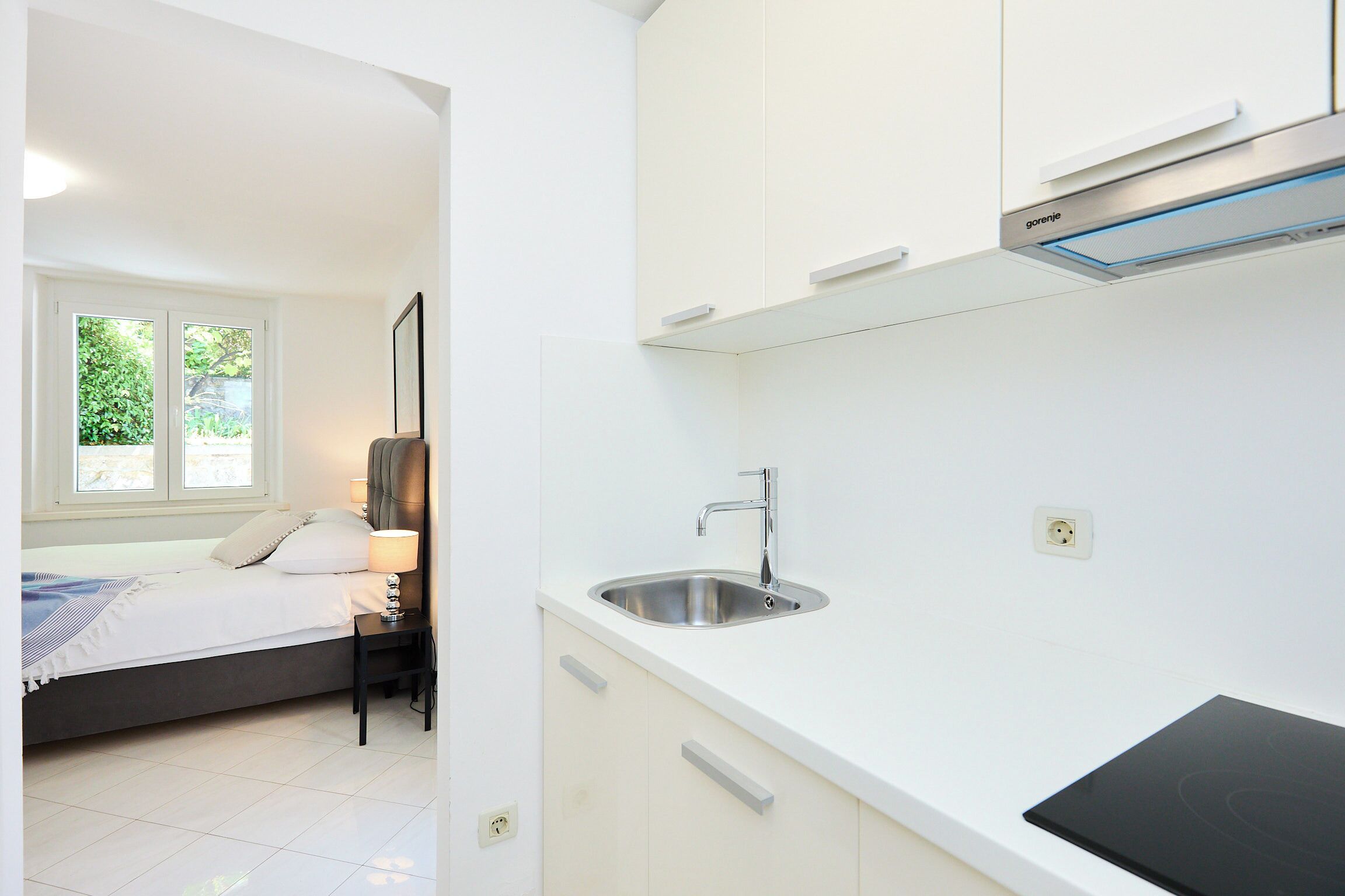 A modern, clean room with a bed, bedside table, and a built-in sink.
