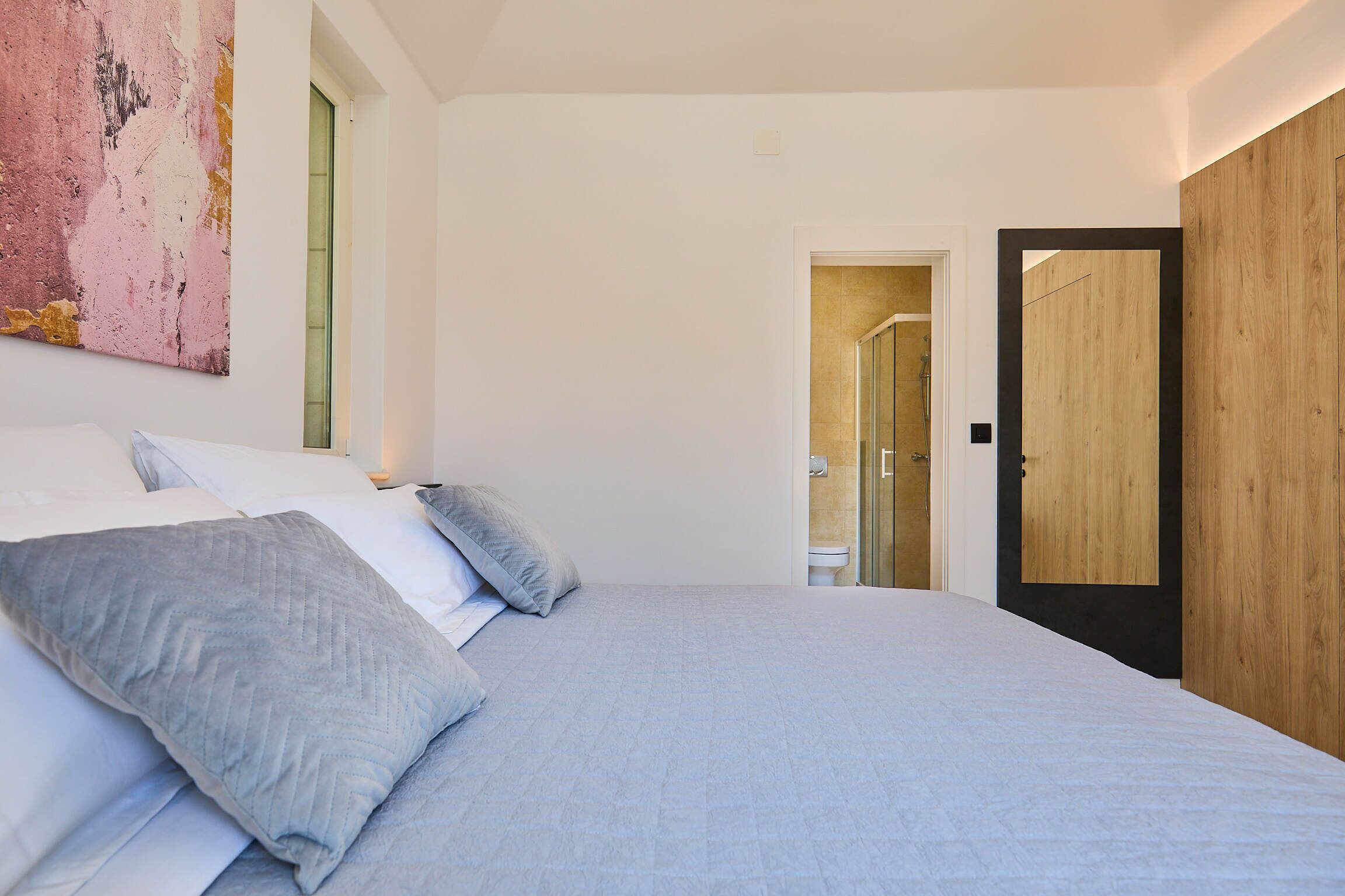 Une chambre à coucher avec un grand lit, une porte en bois et une salle de bain visible à travers une porte ouverte.