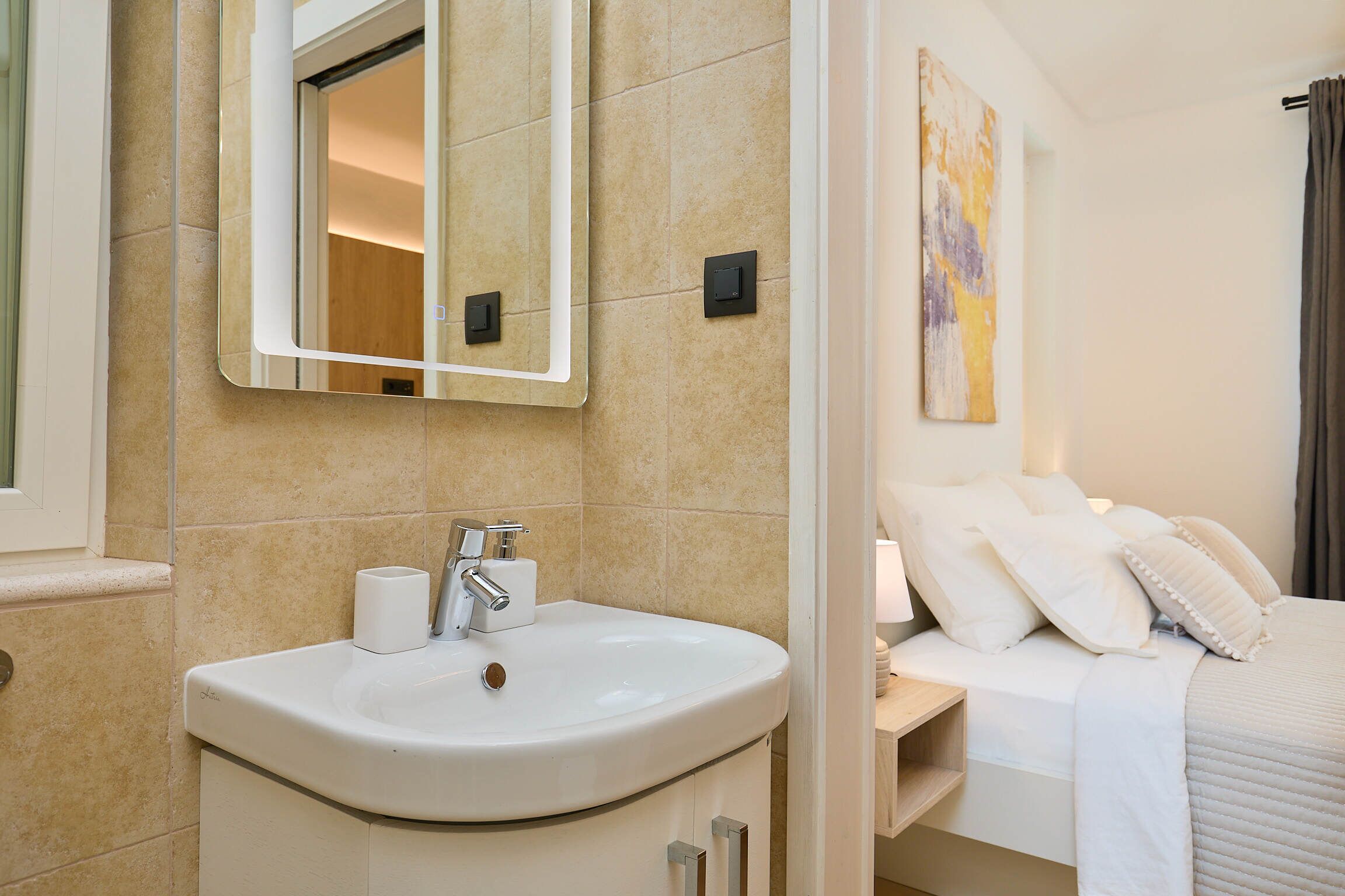A bathroom with a sink, mirror, and a bed with pillows.