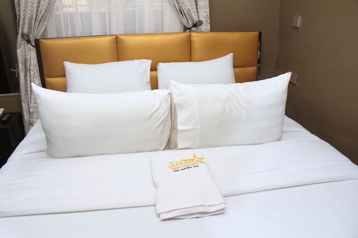 A neatly made bed with white linens and pillows, a folded towel with text, and a headboard with a gold finish.