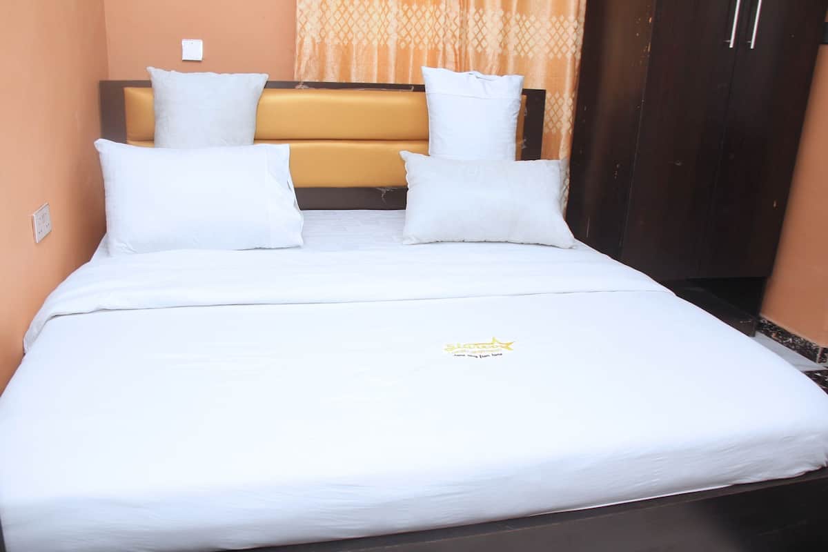 A neatly made bed with white bedding and pillows, a headboard with a patterned design, and a small logo on the bedspread.