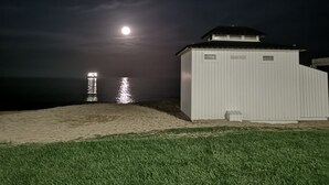 A white building with a black roof, labeled "BLUE FISH," near a beach at night with a visible moon and reflections on the water. - AMAZING VILLA with, chimney, heating, private swimming pool & great views. (Calonge)