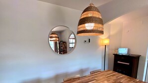 A dining area with a wooden table, a woven pendant light, a round mirror, and a lamp on a stand. - AMAZING VILLA with, chimney, heating, private swimming pool & great views. (Calonge)