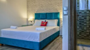 Una habitación de hotel con cama, pared de ladrillo, cabecera color turquesa y mesita de noche con lámpara.