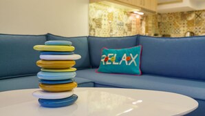 Una pila de platos de colores sobre una mesa blanca en una habitación con un sofá azul y un cojín con la palabra 'RELAX'.