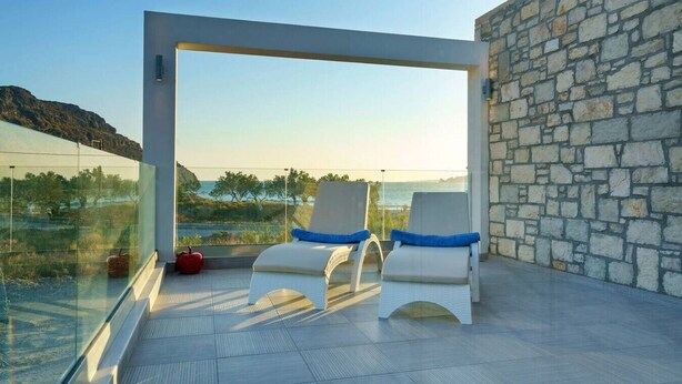 Un balcón con dos sillones de descanso, un muro de piedra y una vista despejada del mar.