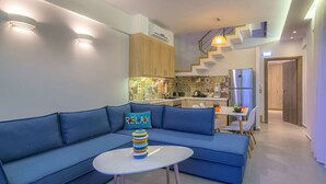 Una sala moderna con un sofá azul, una mesita redonda y una cocina al fondo.