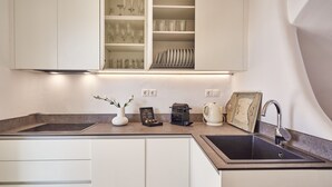 Una cocina moderna con armarios blancos, un lavamanos doble y una encimera con cafetera, hervidor y objetos decorativos.