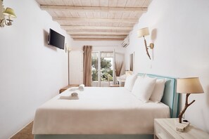 A hotel room with a bed, a TV, a lamp, and a view of the outdoors. - Villa Petrolefko (Mykonos)