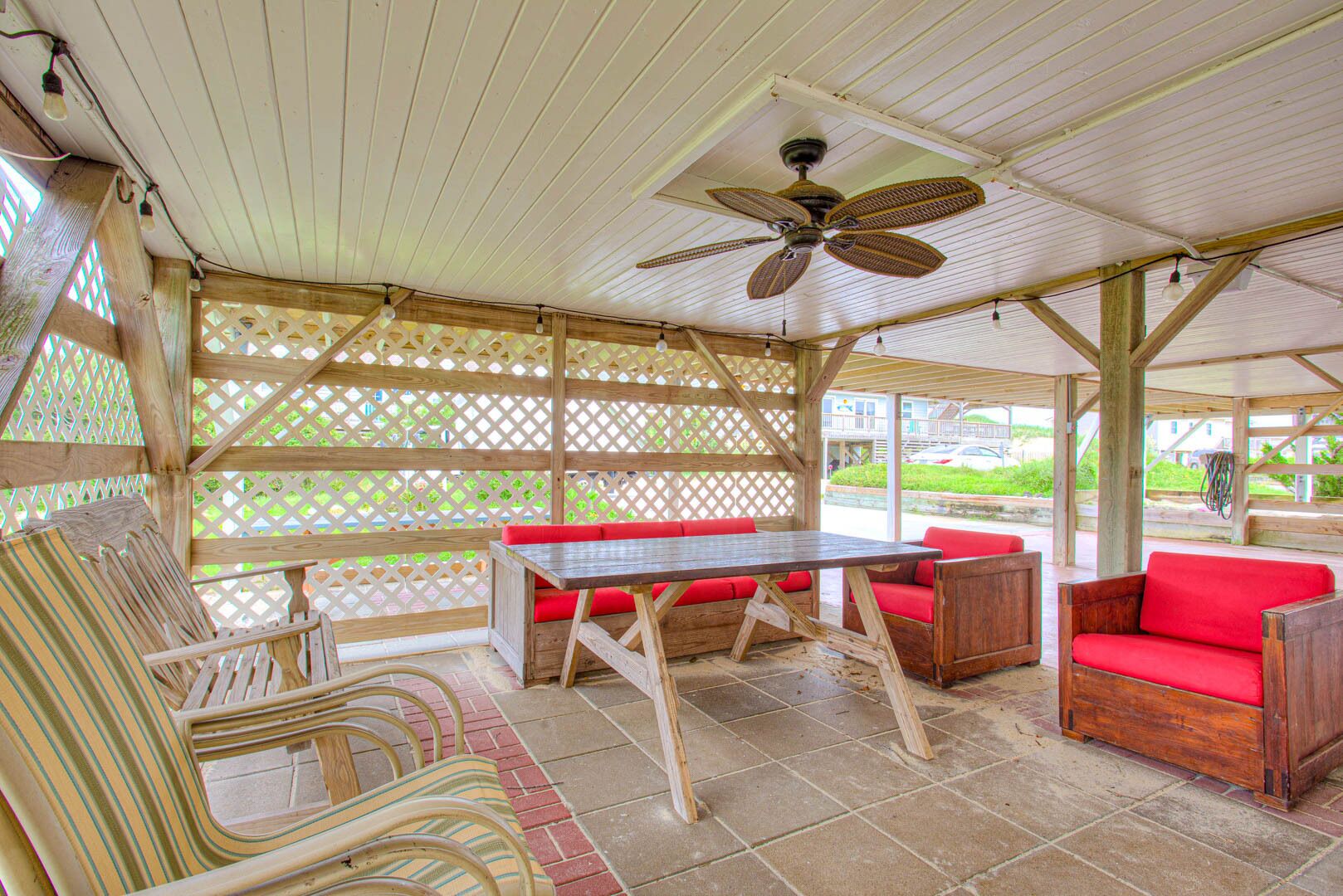 Une terrasse extérieure couverte, aménagée avec des meubles en bois, une table et un ventilateur de plafond.