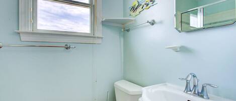 A bathroom with a toilet, sink, and window.