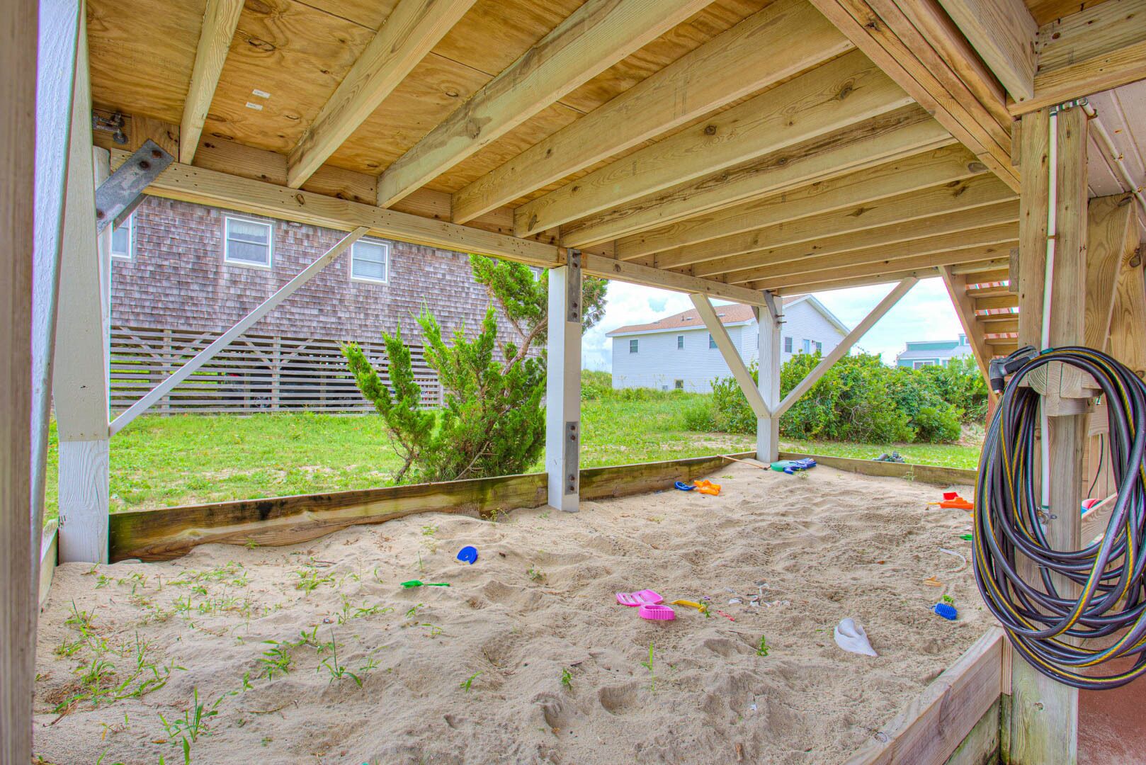 Un espace extérieur abrité, doté d’un sol sablonneux, de poutres en bois et, au fond, d’une maison en briques.
