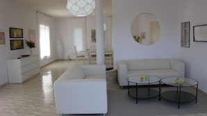 A modern living room with a white sofa, two round glass tables, and a large pendant light.