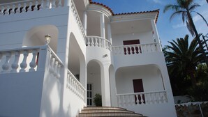 A white building with multiple balconies, a staircase, and a palm tree in the background.