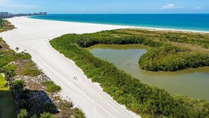 A coastal landscape with a beach, a road curving along the shore, and a body of water. - Beachfront 2BR/2BA condo with heated pool, WiFi, and Marco Island views. (Marco Island)