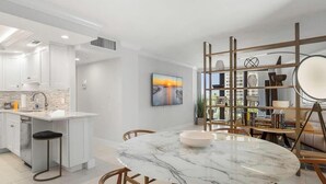 A modern kitchen with white cabinetry, a marble island, and a dining area with a round table and chairs. - Beachfront 2BR/2BA condo with heated pool, WiFi, and Marco Island views. (Marco Island)