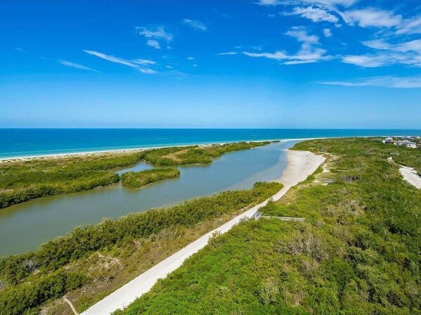 A coastal landscape with a narrow waterway, dense greenery, and a clear blue sky.