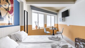 Una habitación de hotel con una cama, una mesita con sillas, un televisor en la pared y una ventana con vistas al exterior.