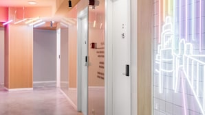 Un pasillo moderno de hotel con suelo de madera, una puerta blanca con el número 15 y una instalación de luces de neón en la pared.