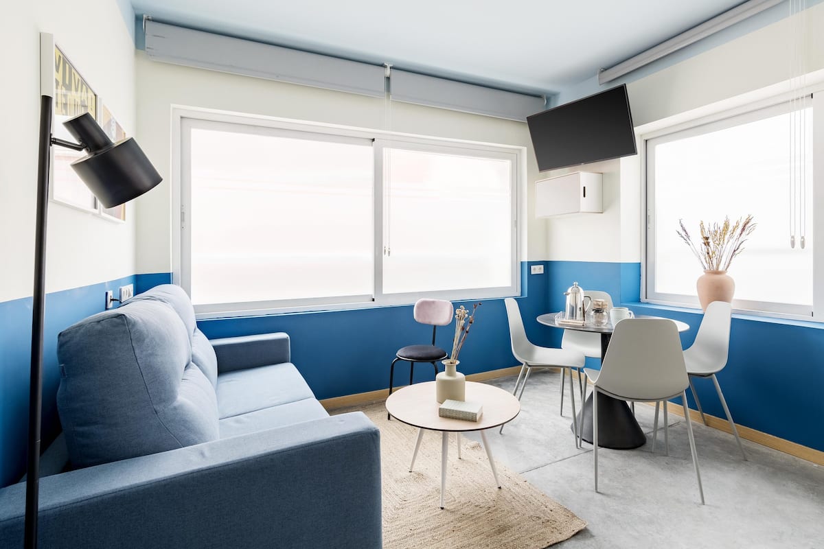 Una sala de estar moderna con una paleta de colores azul y blanco, que incluye un sofá, una mesa redonda de centro y un comedor con sillas y una mesita.