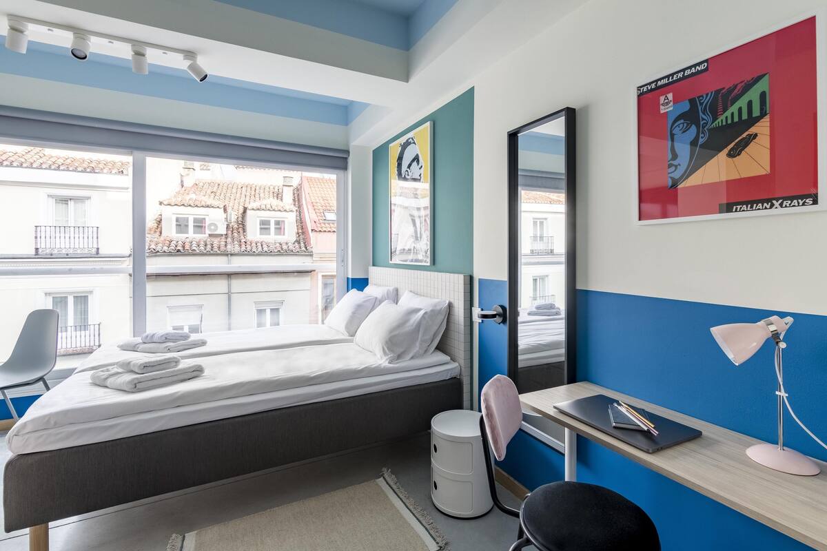 Una habitación de hotel moderna con cama, escritorio, silla y ventanas amplias.