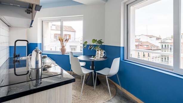 Una cocina moderna con encimera negra, sillas blancas y ventanal con vistas a la ciudad.