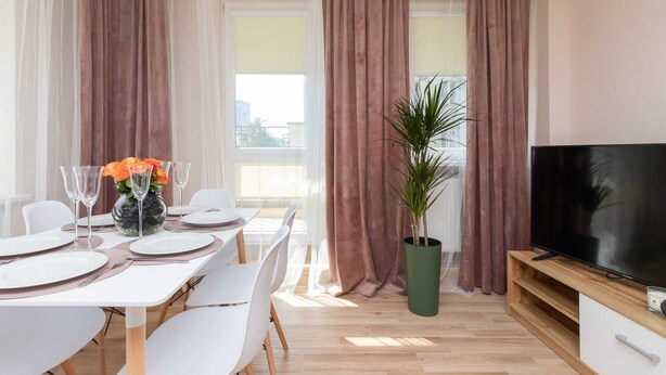 Un comedor moderno con una mesa dispuesta para cuatro, una planta en maceta y un televisor sobre un mueble de madera.