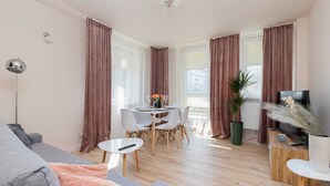 Una sala de estar moderna con un sofá gris, una mesita redonda y un comedor con una mesa y sillas blancas.