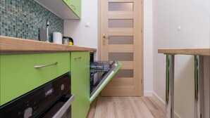Cocina compacta con lavavajillas, una puerta de madera y un armario verde.