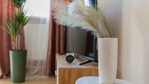 Una habitación con un mueble de televisión de madera, un florero blanco con plumas de plumero y una planta verde en maceta.