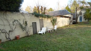 A grassy backyard with a white wall, a metal gate, and outdoor furniture. - RENAISSANCE cottage (Courchamps)