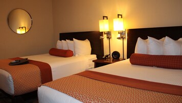 Habitación de hotel con dos camas, cada una con ropa blanca y detalles rojos, un espejo redondo en la pared y dos lámparas fijadas a la pared.