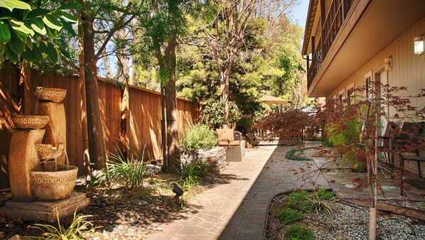 A courtyard with a stone pathway, wooden fence, and outdoor furniture. - The Zen Hotel (Palo Alto)
