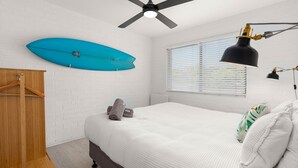 Ein Schlafzimmer mit Bett, Deckenventilator, Surfbrett, Fenster mit Jalousien und einem Holzschrank.