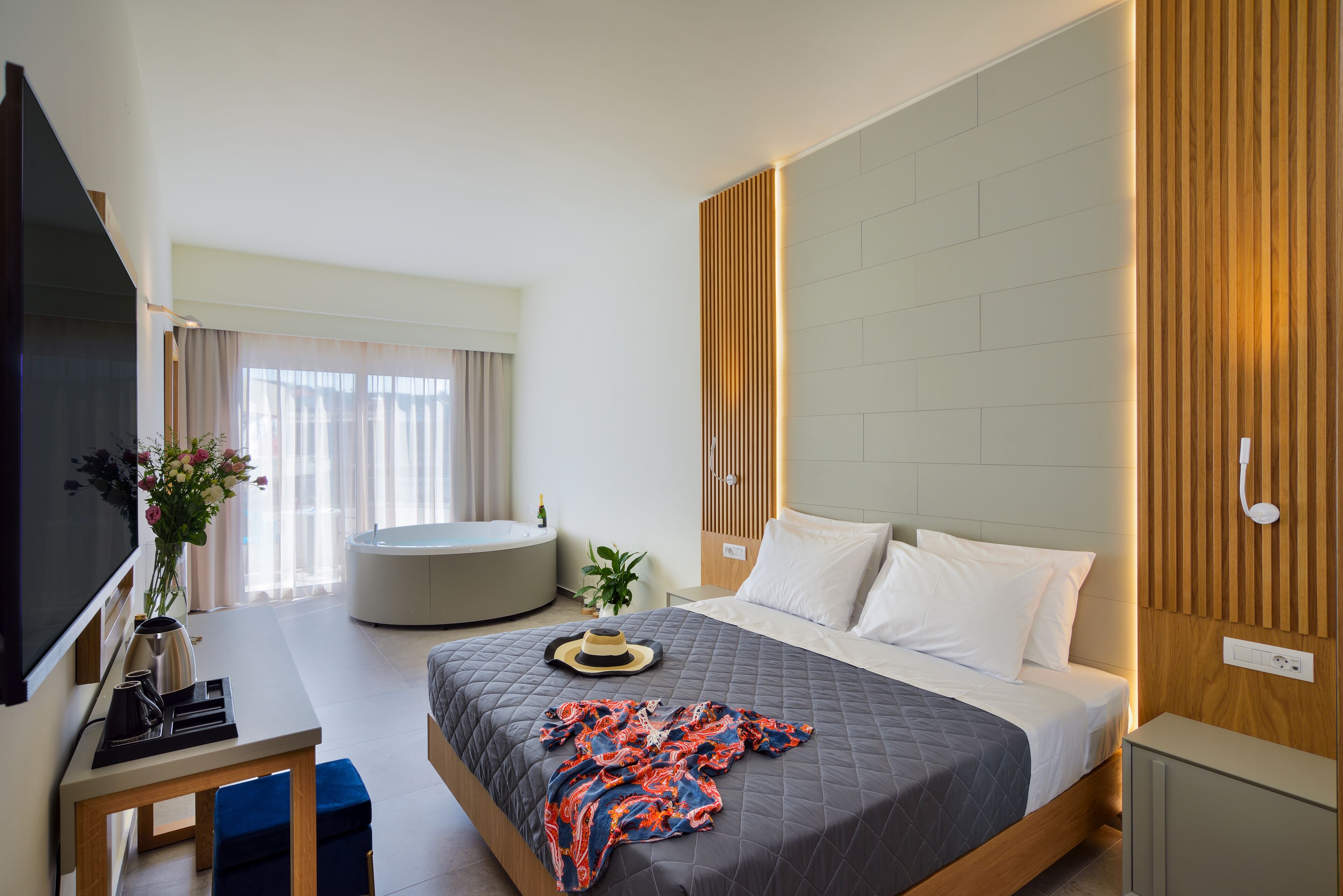 A modern hotel room with a large bed, a flat-screen TV, a desk, and a seating area.
