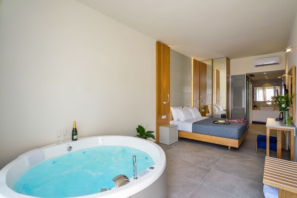 A modern bedroom with a large bathtub, a bed, a bedside table, and a mirror.