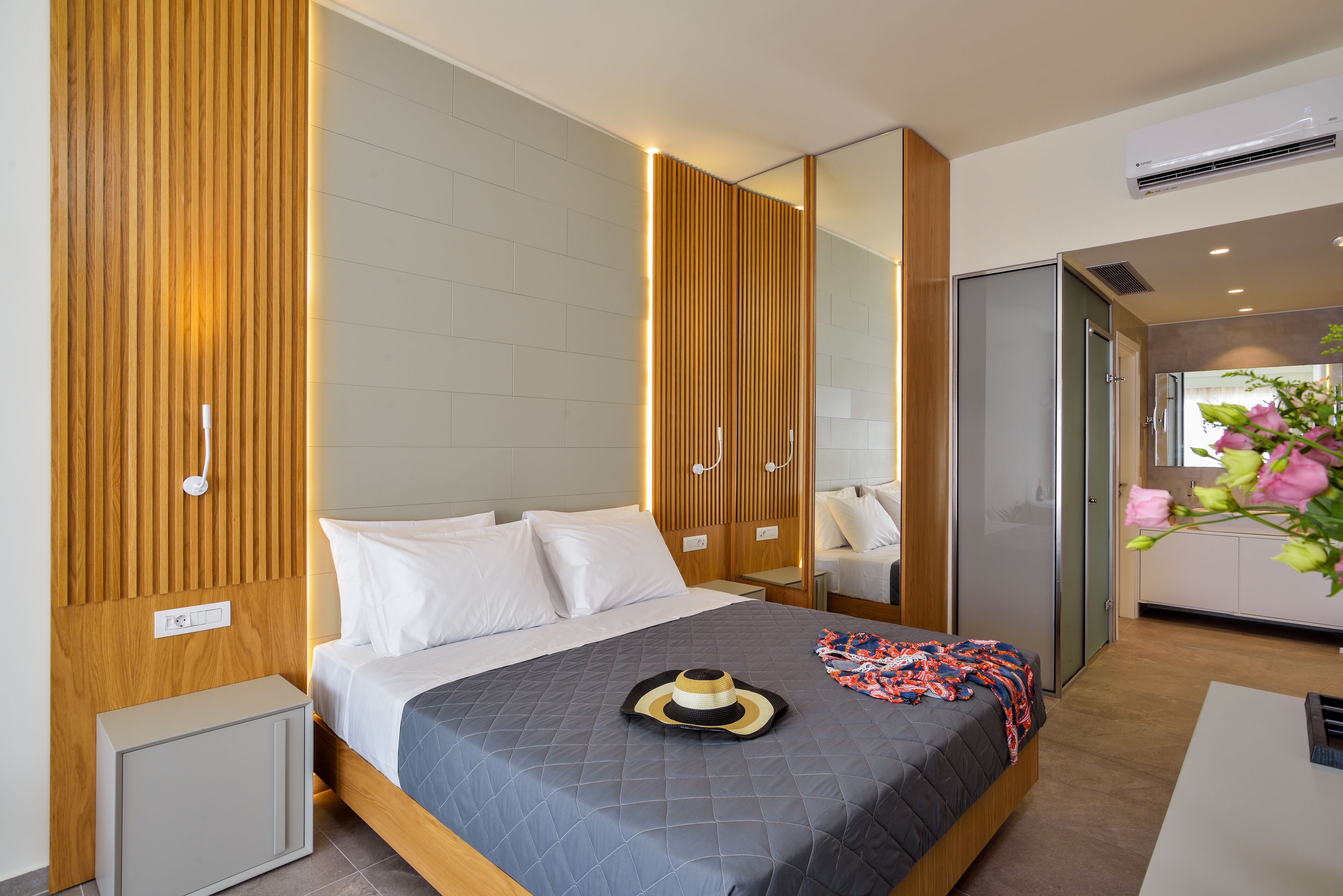 Une chambre d’hôtel moderne avec un grand lit, des panneaux de bois au mur, une petite table de chevet, un miroir et un coin cuisine.