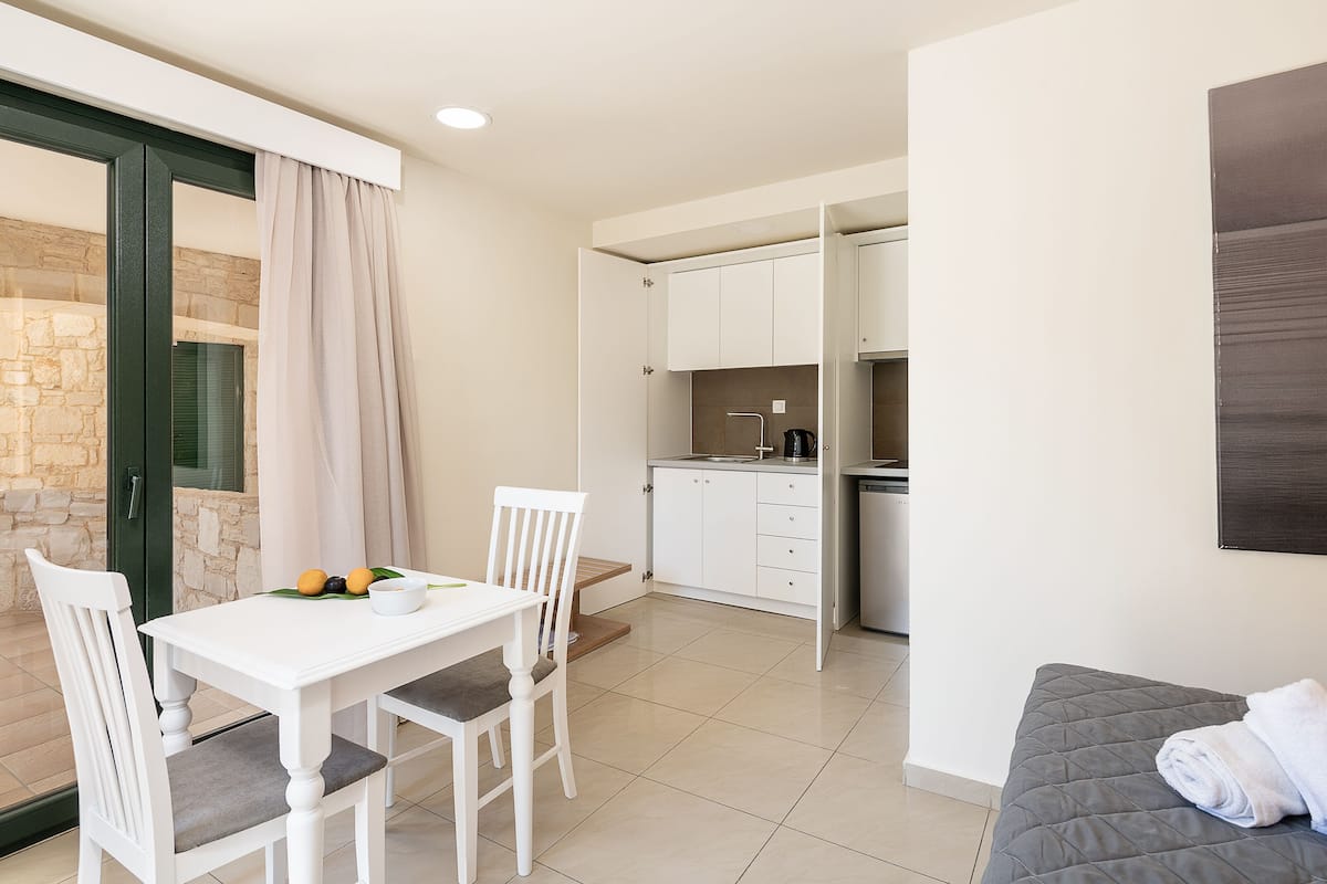 A compact room with a dining table, chairs, a grey sofa, and a kitchenette.