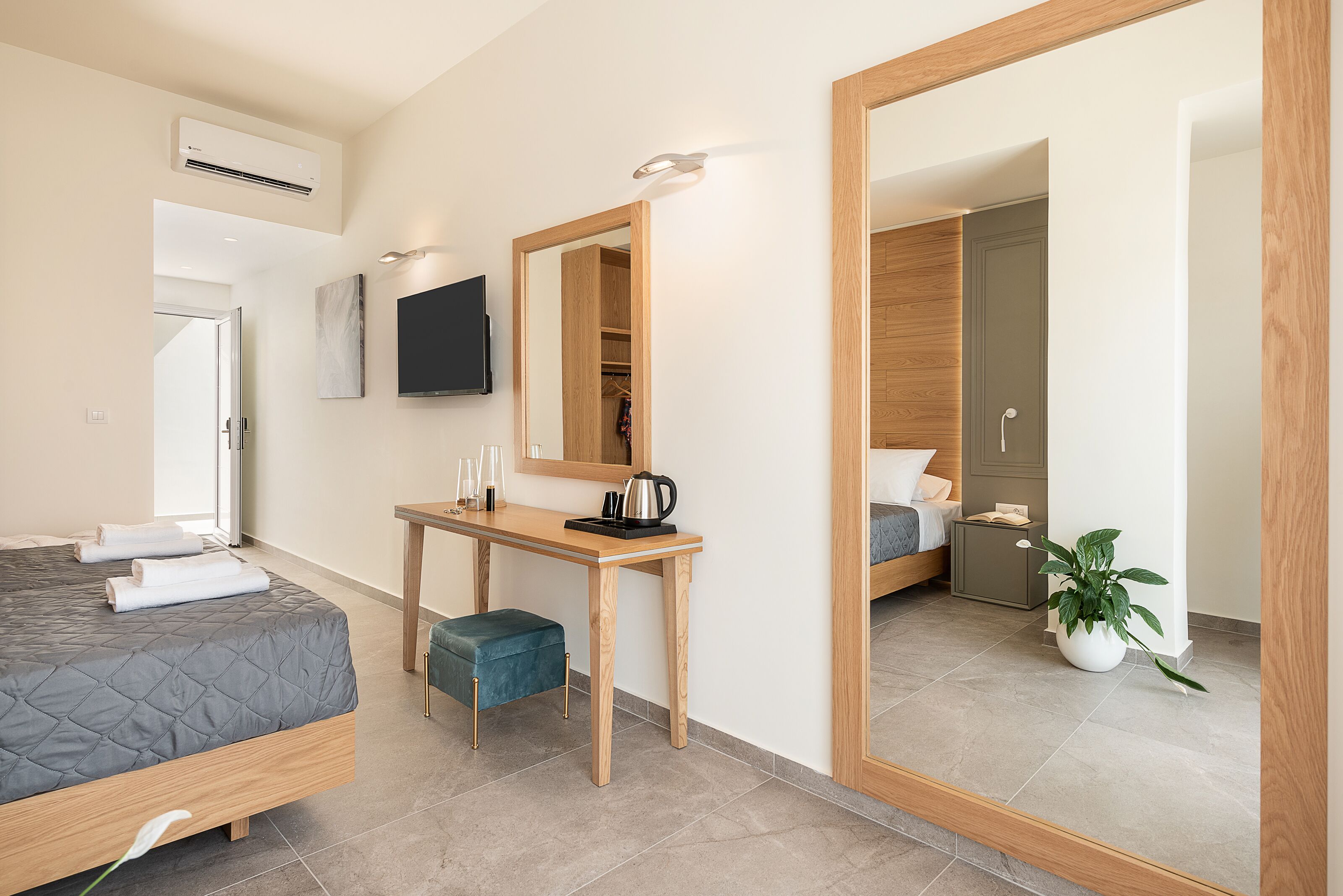 Una habitación de hotel moderna con una cama, un escritorio, un espejo, un televisor y una planta en maceta.