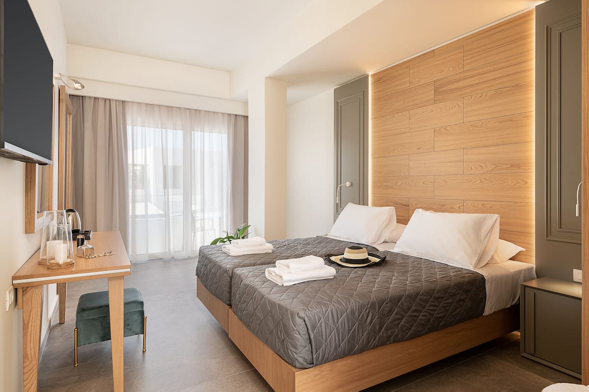 A modern hotel room with a large bed, a desk with a chair, a television, and a wardrobe.