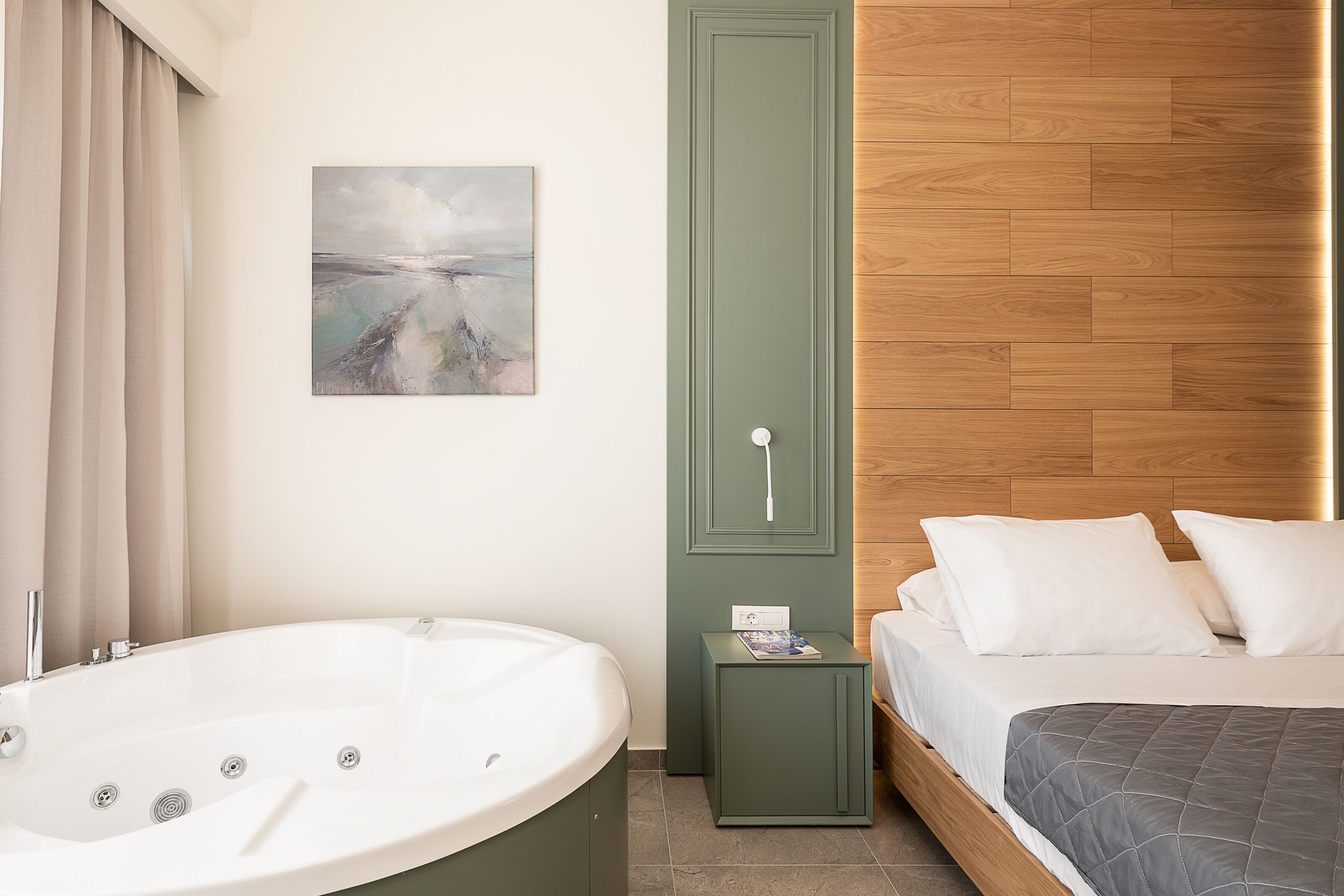 A modern bedroom with a large bathtub, a wooden headboard, a small bedside table, and a painting on the wall.