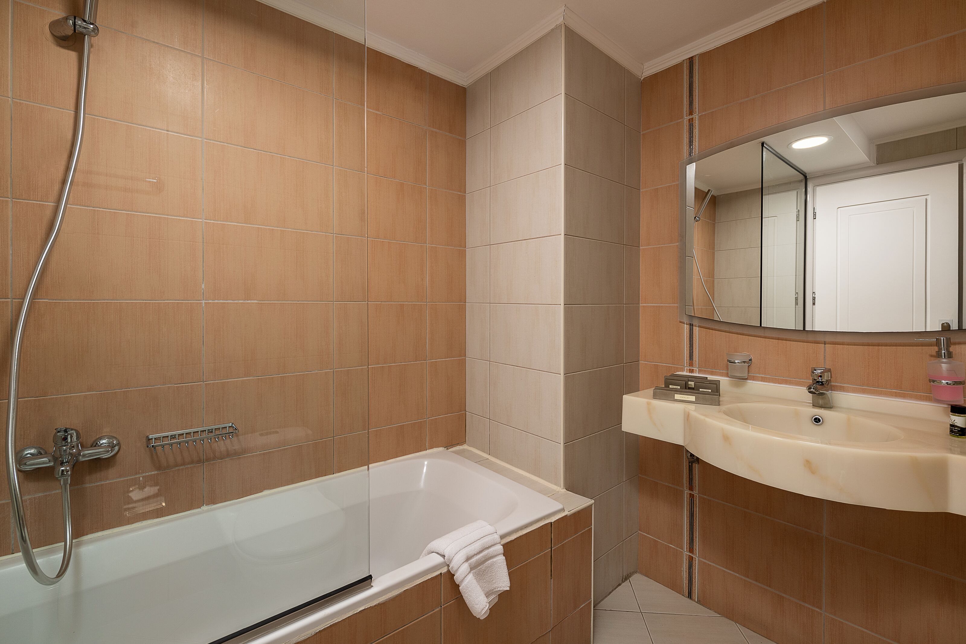 A bathroom with a glass-enclosed bathtub, a sink with a mirror above it, and wooden wall tiles.