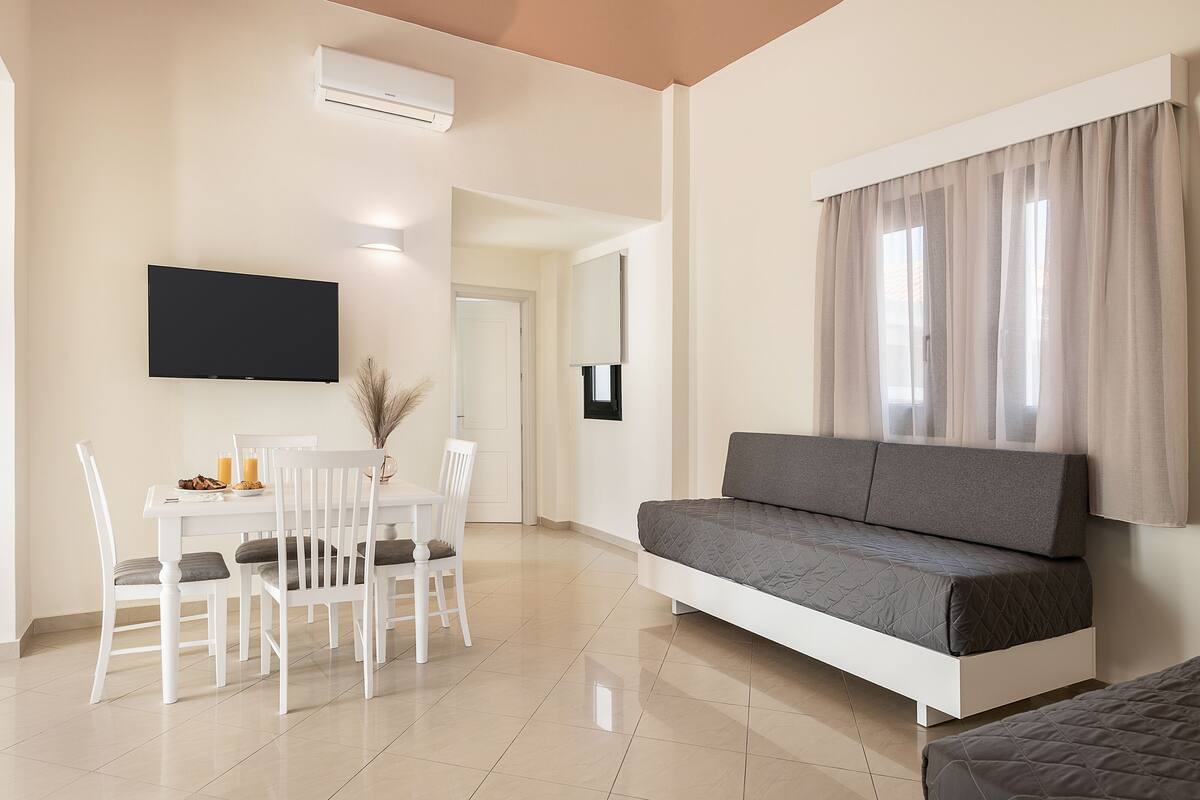 A modern living room with a sofa, dining table, chairs, and a flat-screen TV.