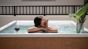 A person relaxing in a hot tub with a glass of wine and a plant beside them. - Elia Platanias (Platanias)