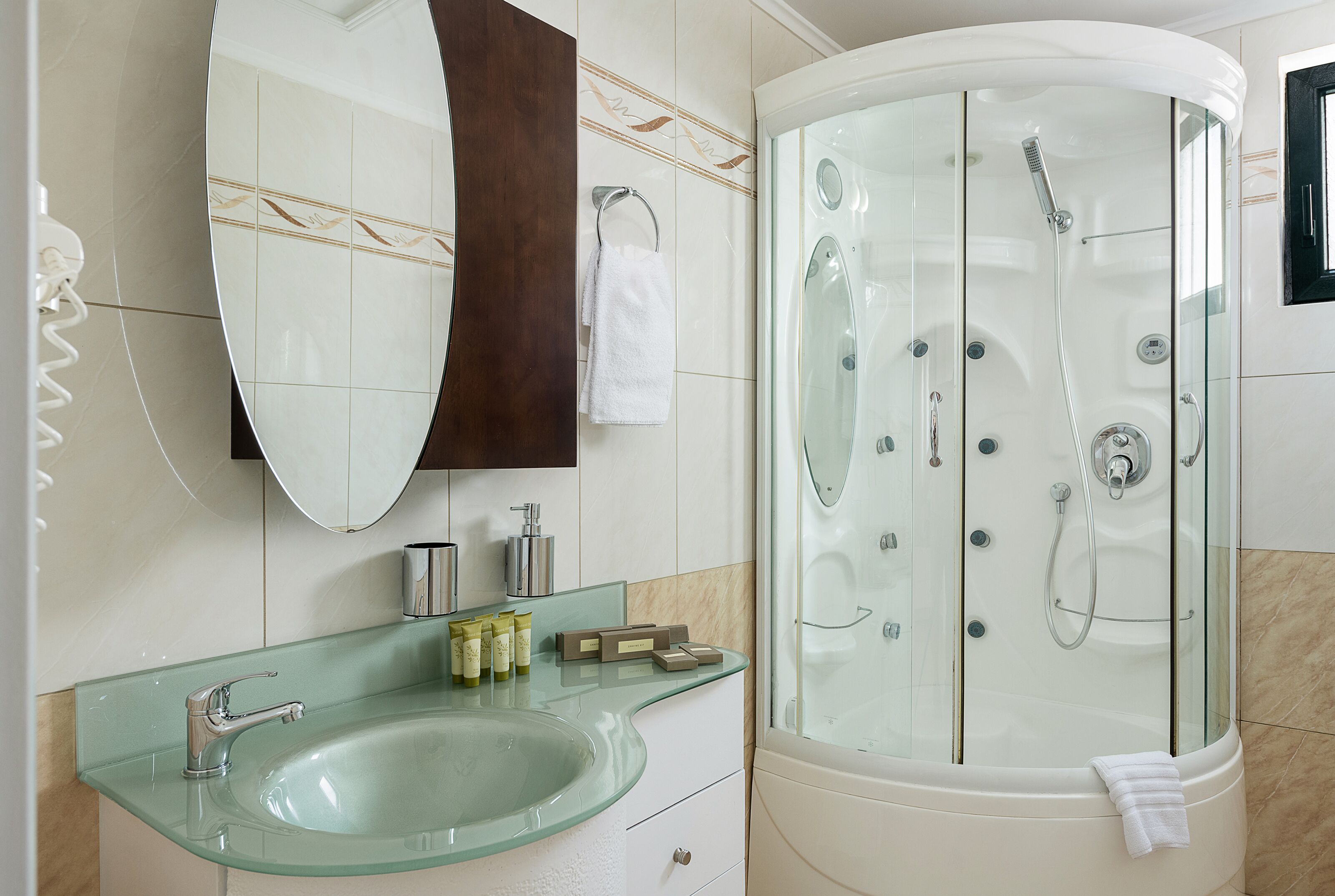 A modern bathroom with a glass sink, a large mirror, a glass-enclosed shower, and a towel hanging on the wall.