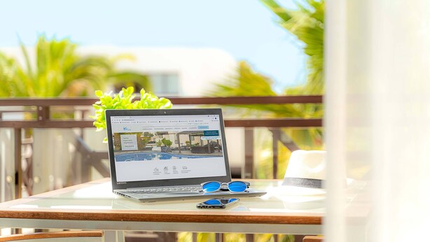 Een laptop op een glazen tafel, met zicht op een zwembad en groen in de achtergrond.