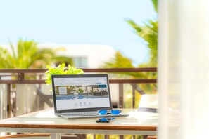 A laptop on a glass table with a view of a pool and greenery in the background. - Natura Volcán by Vitalclass Lanzarote Resort (Costa Teguise)