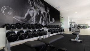 Een sportschool met een muurschildering, dumbbells, banken en trainingsapparatuur.
